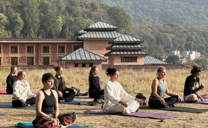 A group of individuals seated in a yoga pose on mats in an outdoor setting.